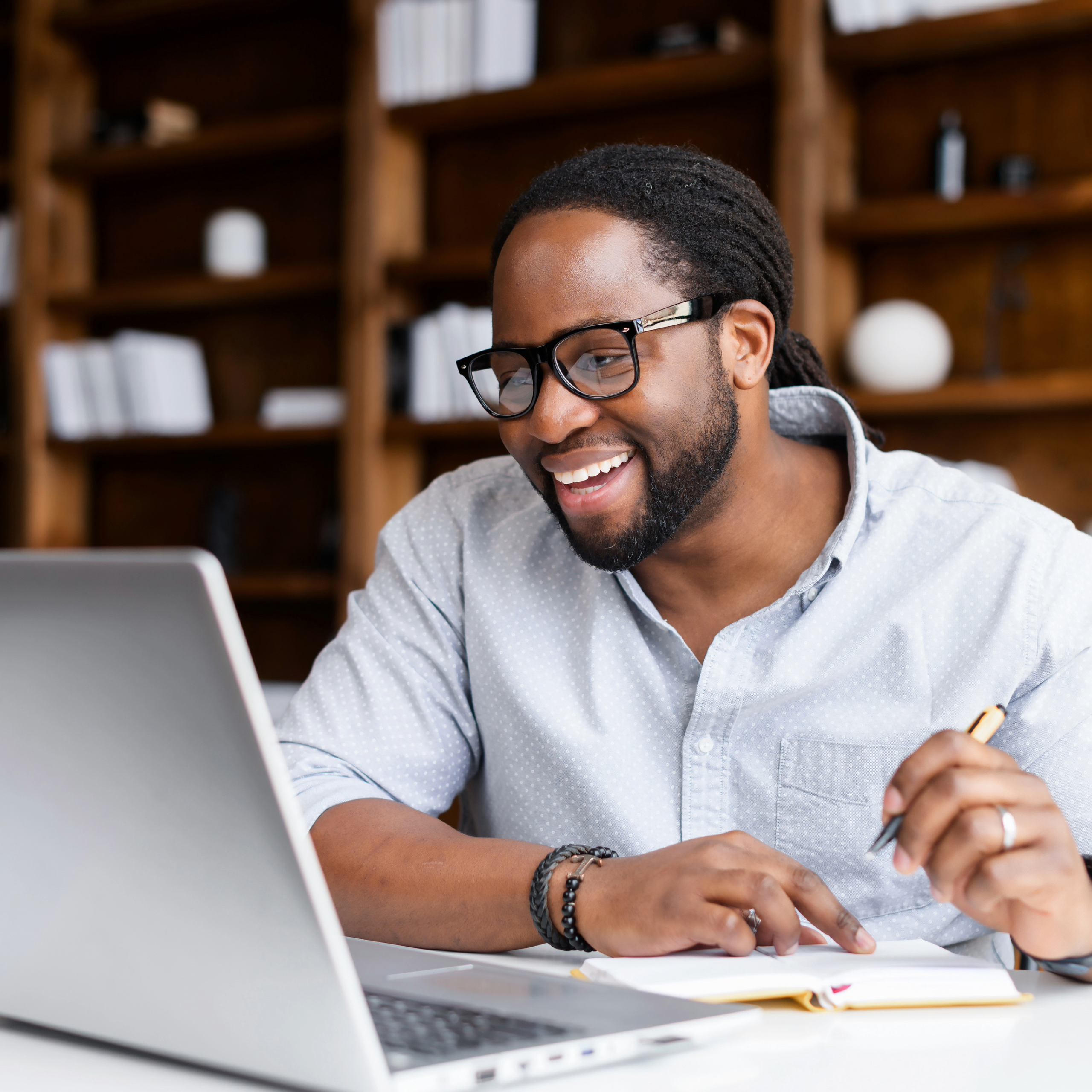 man searching for a new job on his laptop in his office. He is holding a pen and taking notes